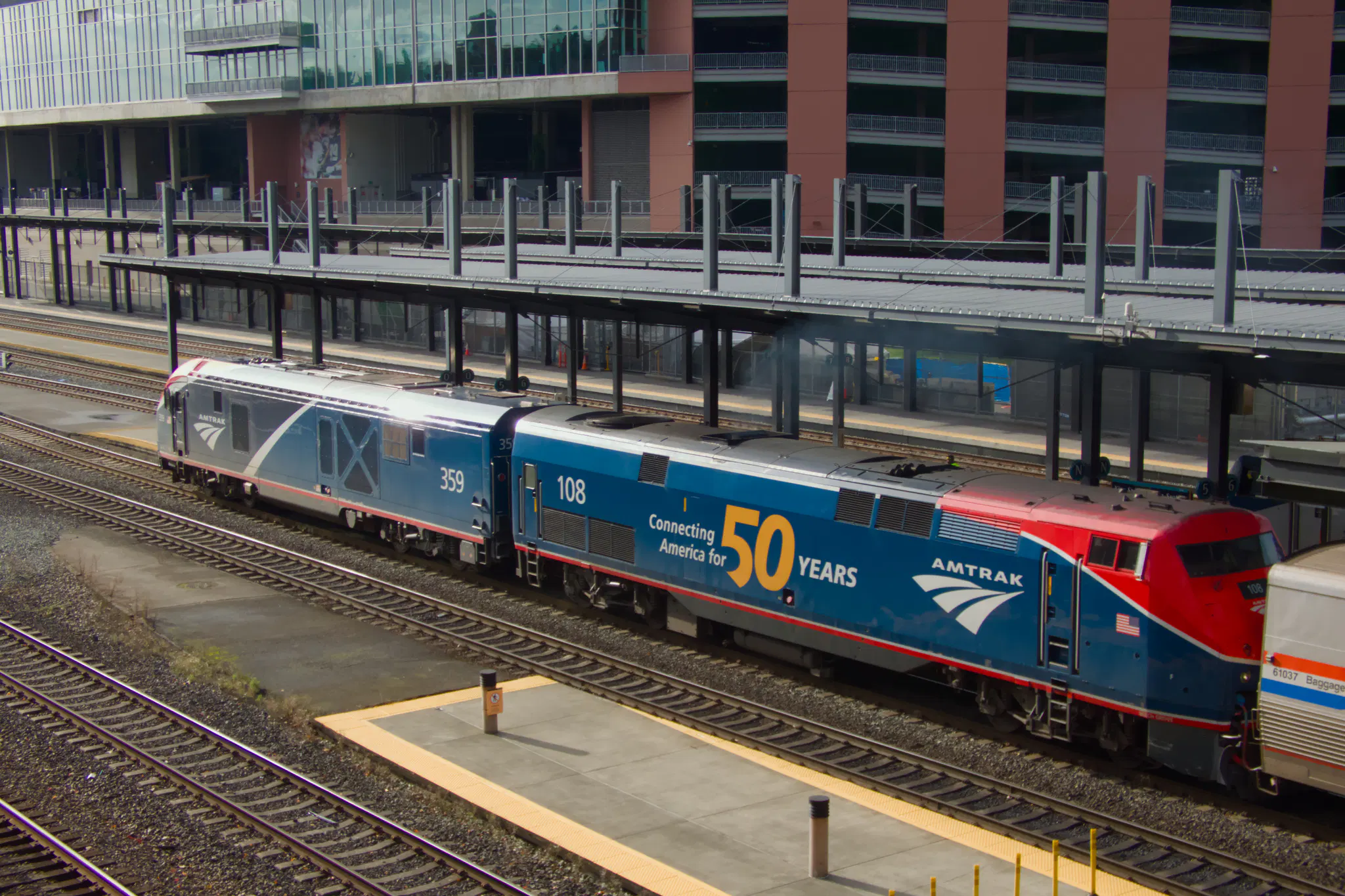 Coast Starlight leaving the station at King Street Station in Seattle.

The lead locomotive is 359, a 2024 Siemens Charger ALC-42, with the newer blue and dar blue livery, with some spots of red and black.

The locomotive right behind it, coupled back-to-back, is number 108, a 1997 GE P42DC Genesis locomotive, with a special livery. It's mainly blue, with red on the top front around the cab windows. On the side is "Connecting America for 50 YEARS", with the number 50 being particularly prominent.